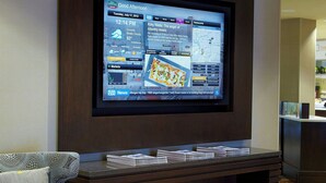 A modern living room with a flat-screen TV mounted on a dark wooden wall, a patterned sofa, and a small entertainment unit with a bowl of apples. - Courtyard by Marriott Buffalo Amherst/University (Buffalo)