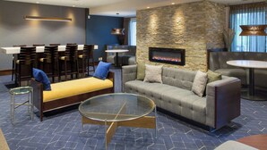 A modern lounge area with a stone wall, a fireplace, a sofa, a round glass coffee table, and a seating area with chairs and tables. - Courtyard by Marriott Buffalo Amherst/University (Buffalo)