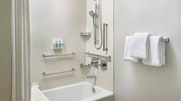 A modern bathroom with a bathtub, shower, and handrails.