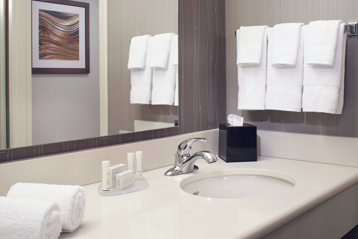 A bathroom with a white sink, a mirror, and towels hanging on the wall.