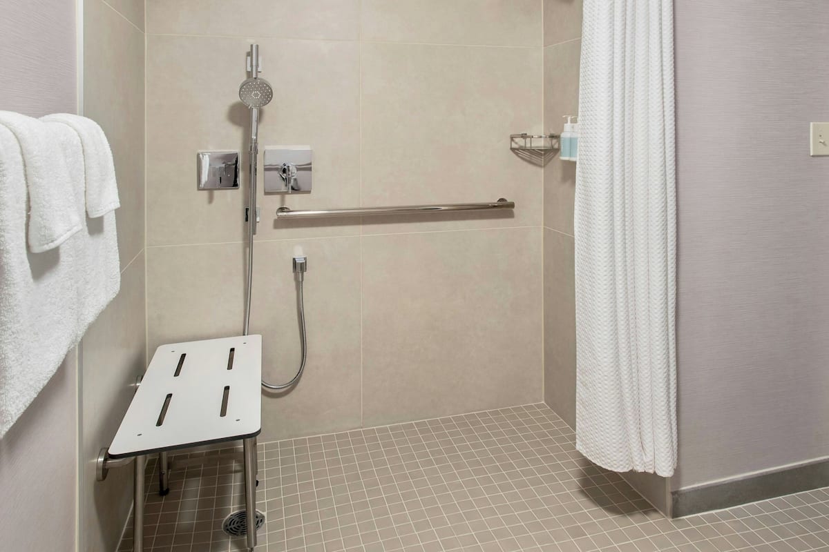Área de duche com barra de apoio, suporte de toalhas e painel de comandos.