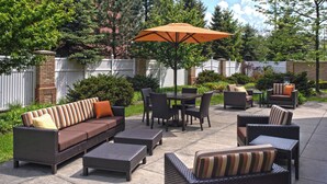 An outdoor patio area with wicker furniture, including sofas, chairs, and a table, under a large umbrella. - Courtyard by Marriott Cleveland Independence (Independence)