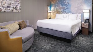 A hotel room with a large bed, a sofa, a nightstand with a lamp, and a wall with a cityscape mural. - Courtyard by Marriott Cleveland Independence (Independence)