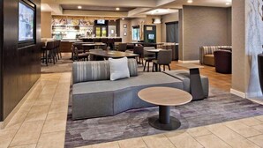 A modern lounge area with seating arrangements, a bar in the background, and a television screen. - Courtyard by Marriott Ballantyne (Charlotte)