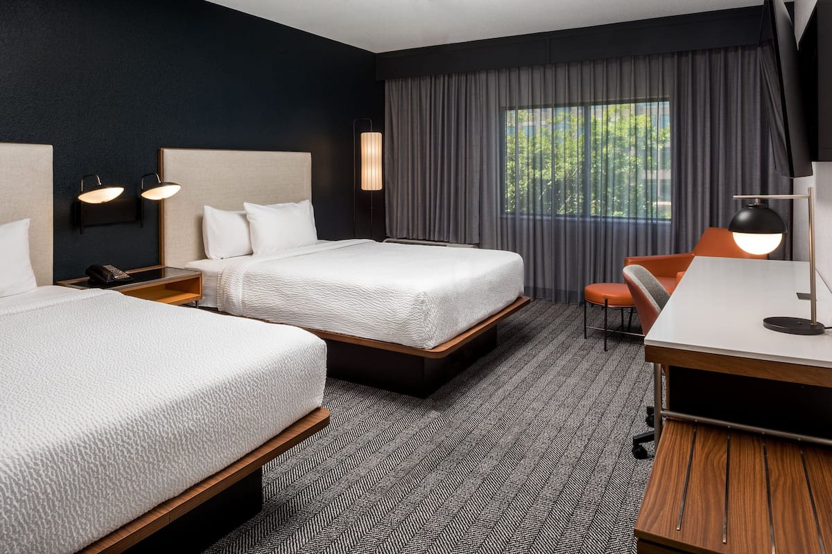 A hotel room with two beds, a desk, and a chair.