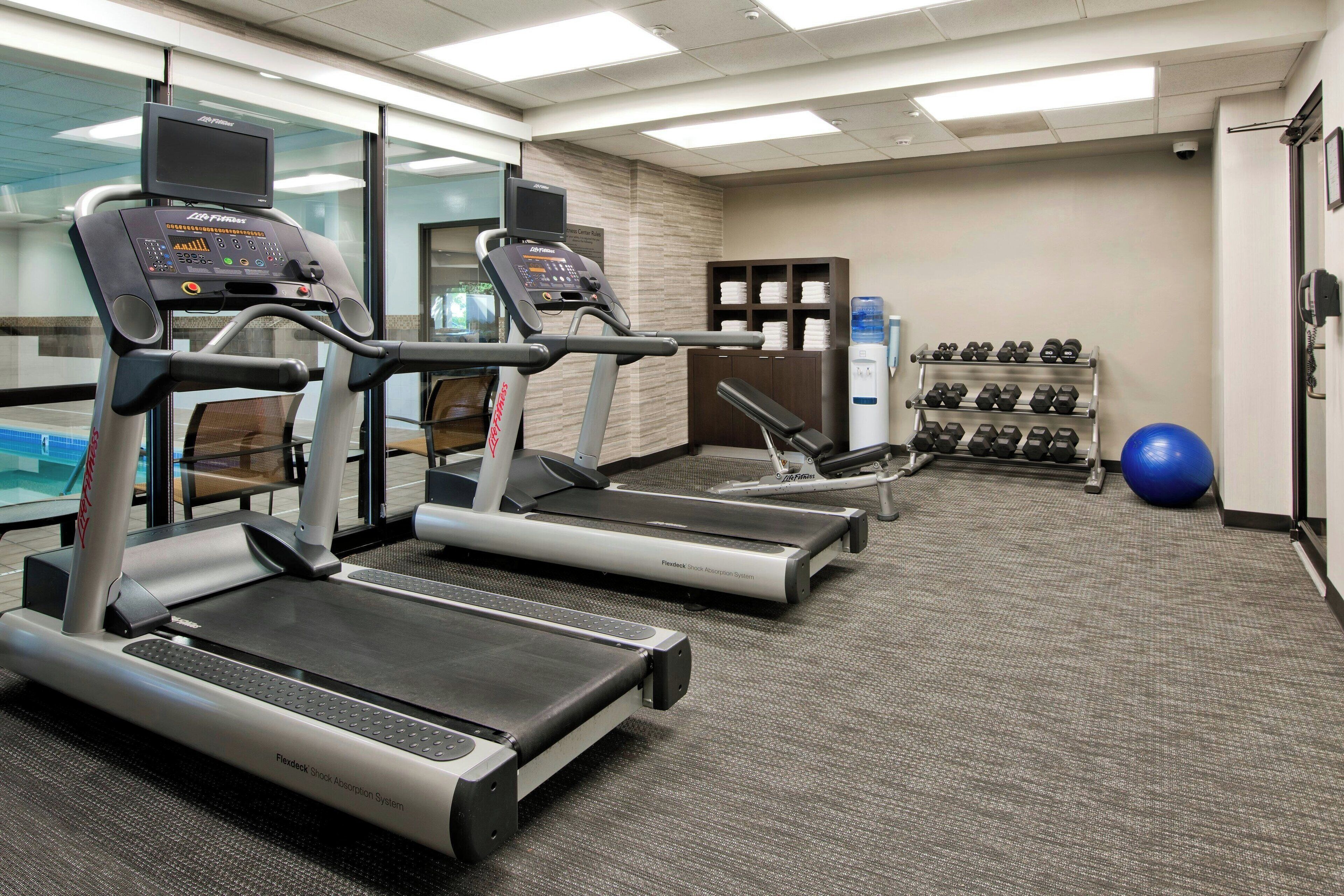 Een fitnessruimte met loopbanden, gewichten en fitnessballen.