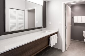 A modern bathroom with a white vanity, dark wood cabinet, and a large mirror. - Courtyard by Marriott Ballantyne (Charlotte)
