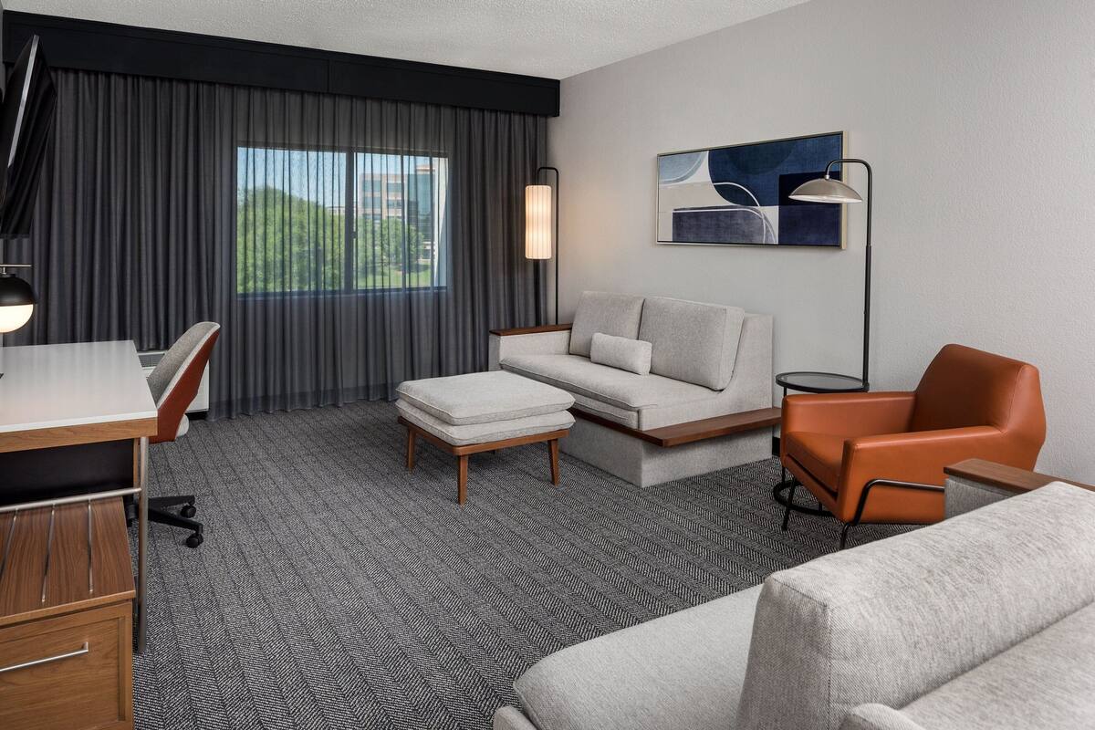 A hotel room with a sofa, armchair, ottoman, desk, and lamp.