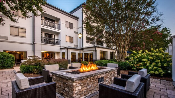 An outdoor patio with a stone fire feature, wicker furniture, and a building with balconies and large windows. - Courtyard by Marriott Ballantyne (Charlotte)