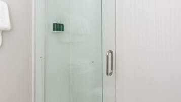 Een douche met glazen wand, een witte betegelde muur en een lichtgekleurde vloer.