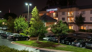 Een Courtyard Marriott hotel met een parkeerplaats en bomen ervoor.