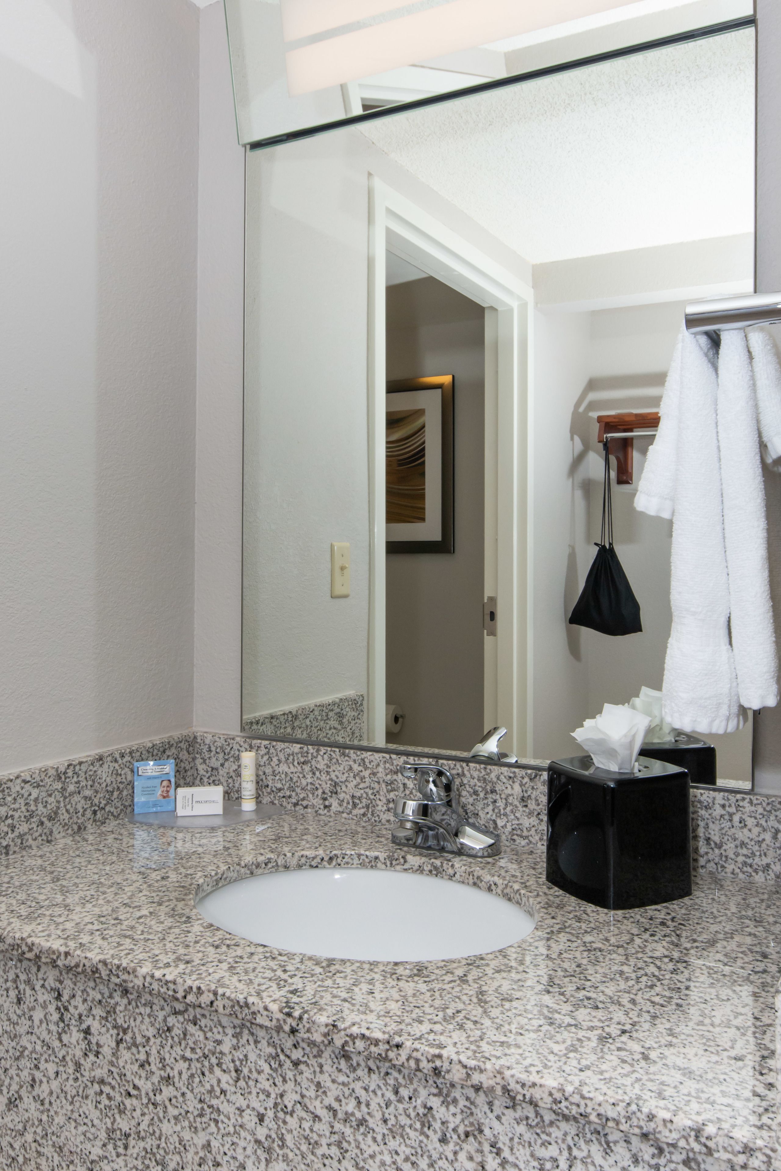 A bathroom with a granite countertop, a white sink, a mirror, and a towel rack with a white towel.