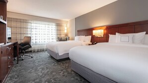Een hotelkamer met twee bedden, een bureau, een stoel en een raam met gordijnen.