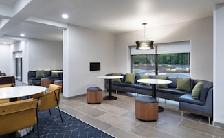 A modern lounge area with seating, tables, and a large window offering a view of the outdoors.