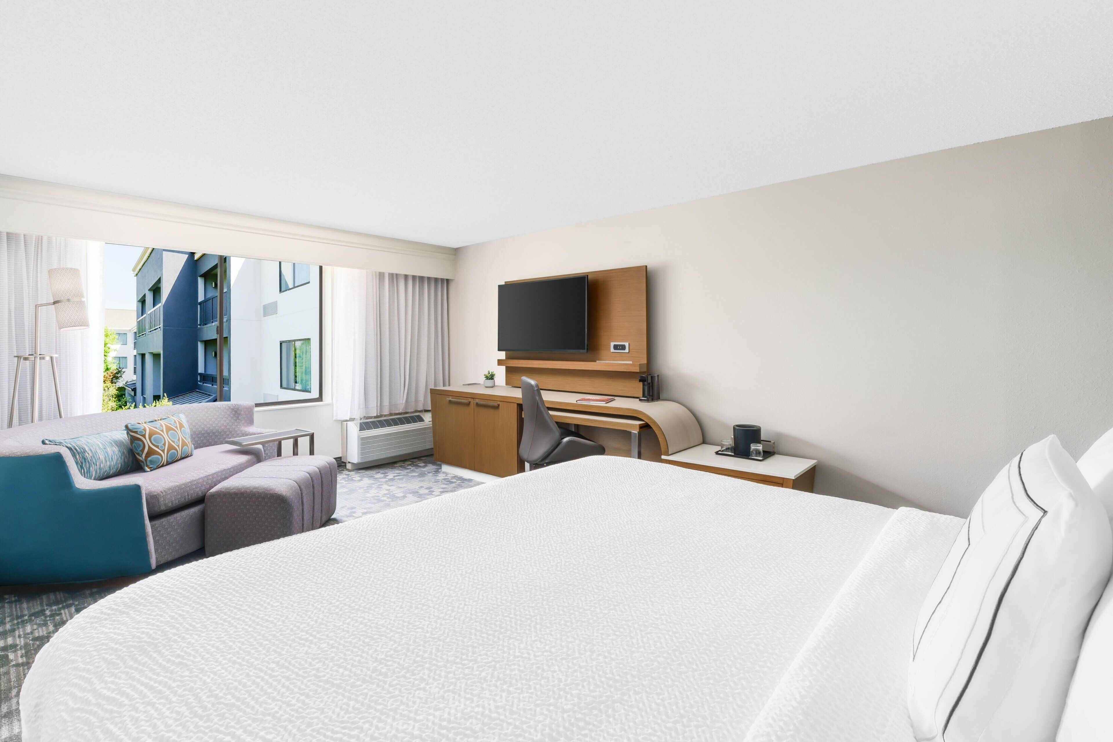 Une chambre d’hôtel avec un grand lit, un bureau, une chaise, une télévision et une vue sur le bâtiment extérieur.