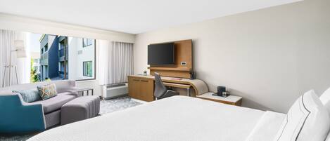 Une chambre d’hôtel avec un grand lit, un bureau, une chaise, une télévision et une vue sur le bâtiment extérieur.