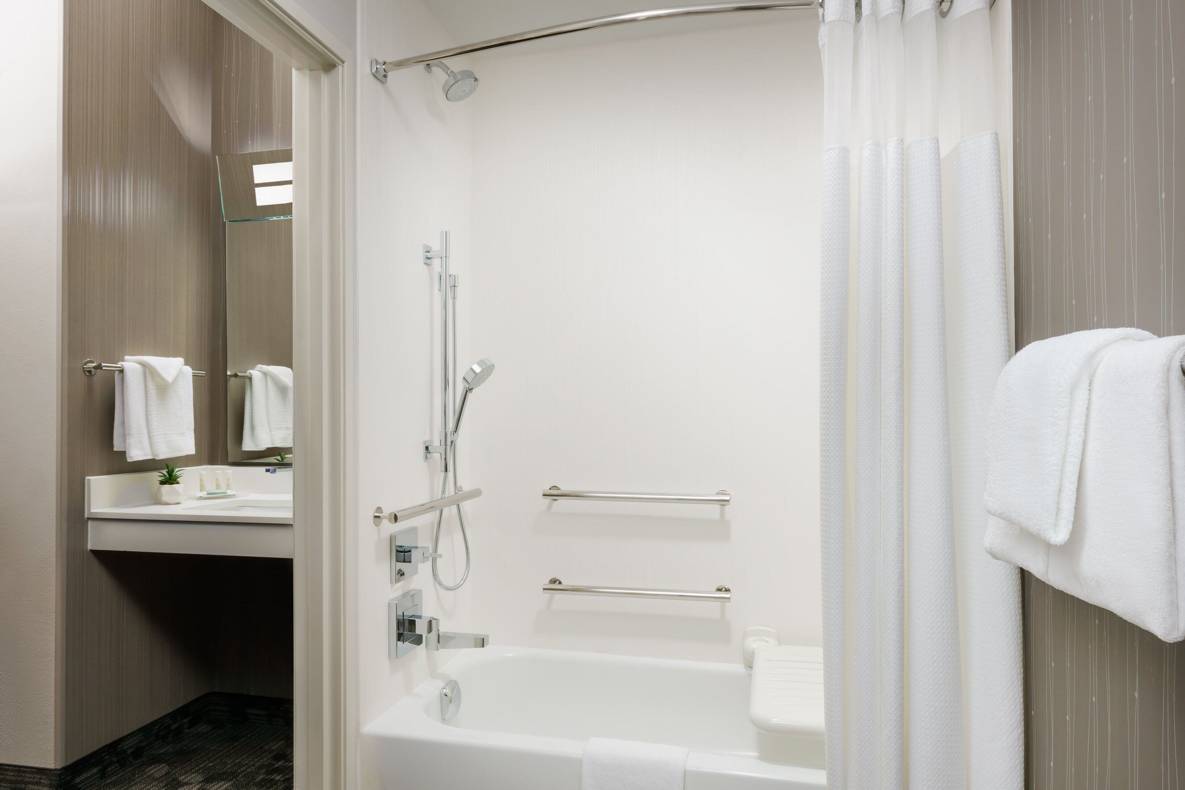 A modern bathroom with a bathtub, shower, and a vanity with a mirror and towel rack.