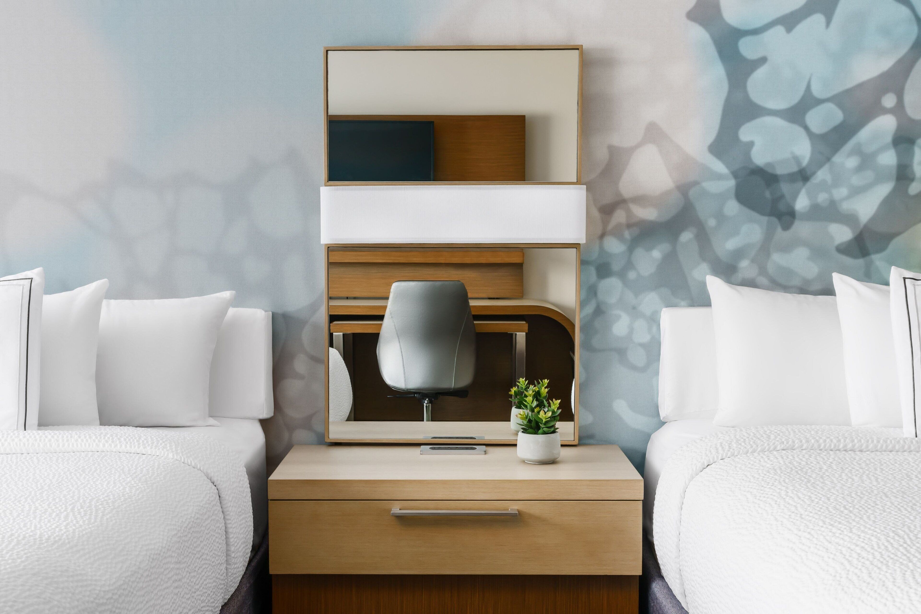 Une chambre d’hôtel avec un lit, un bureau, une chaise, une petite plante et un miroir.