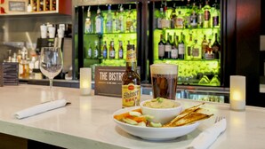 A bar area with a bottle of Shiner Bock beer, a glass of beer, a bowl of dip, and a plate of chips. - Courtyard By Marriott Dallas - Lewisville (Lewisville)