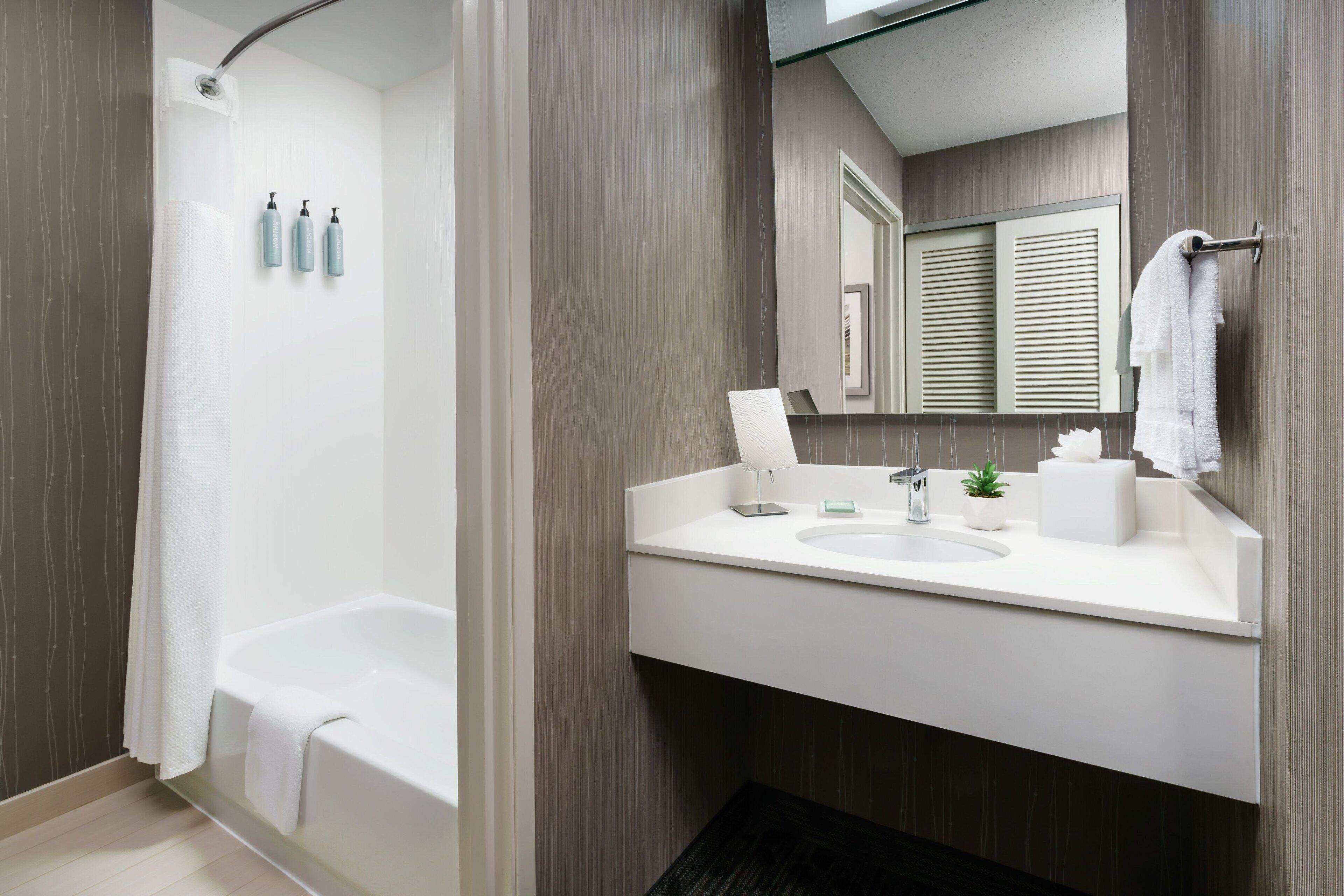 A modern bathroom with a bathtub, a sink with a mirror, and toiletries on the wall.
