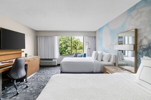 Una habitación de hotel con cama, escritorio, silla, televisor y ventana con cortinas.