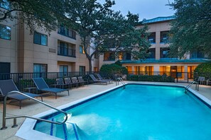 Relax by the pool surrounded by lounge chairs and tables, with a hotel building offering stunning views from its balconies.