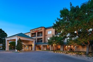 Experience the sleek, modern design of this hotel, featuring a flat roof and central entrance, surrounded by lush greenery and a covered parking area.