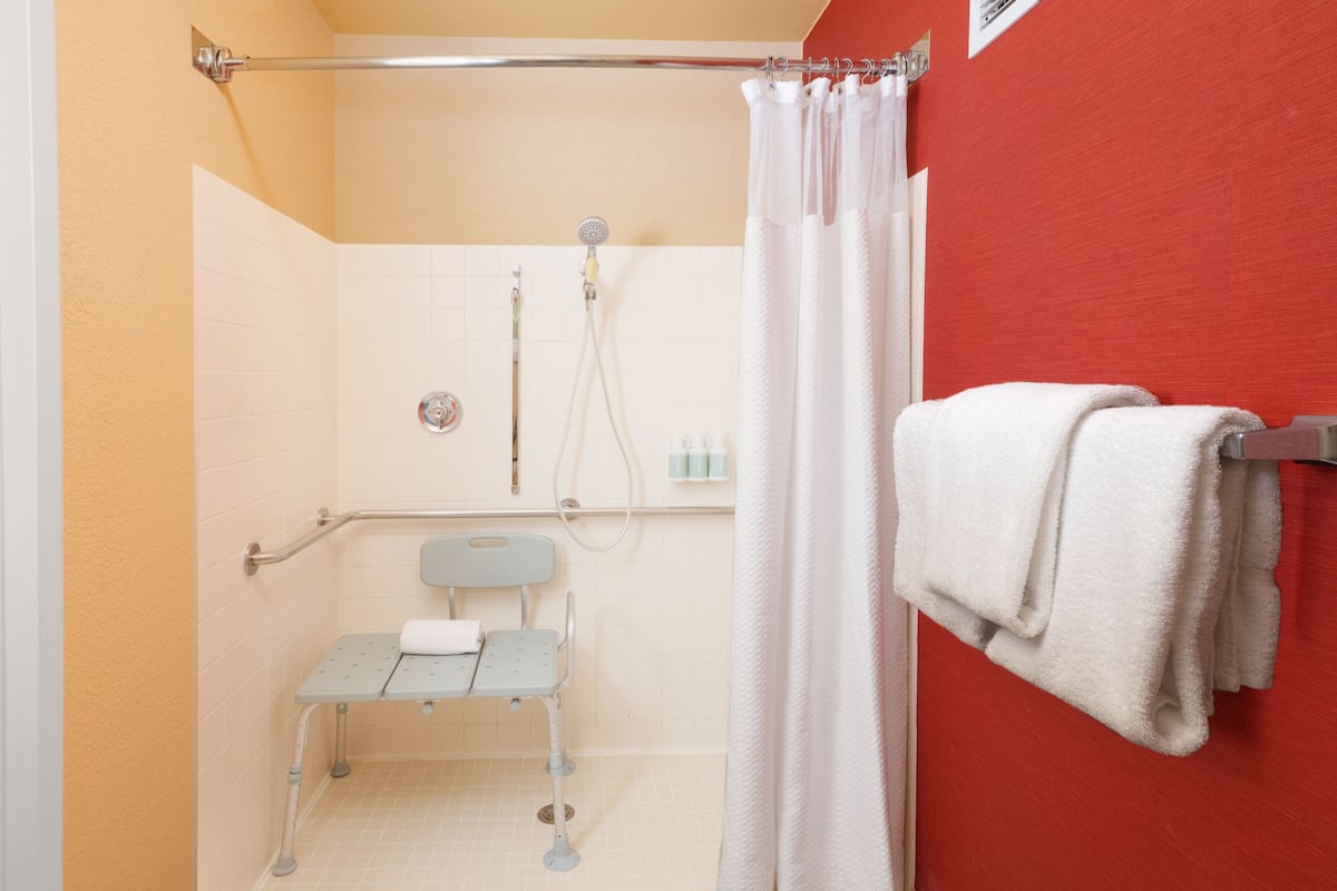 A bathroom with a shower, a wheelchair-accessible bench, and a towel rack.