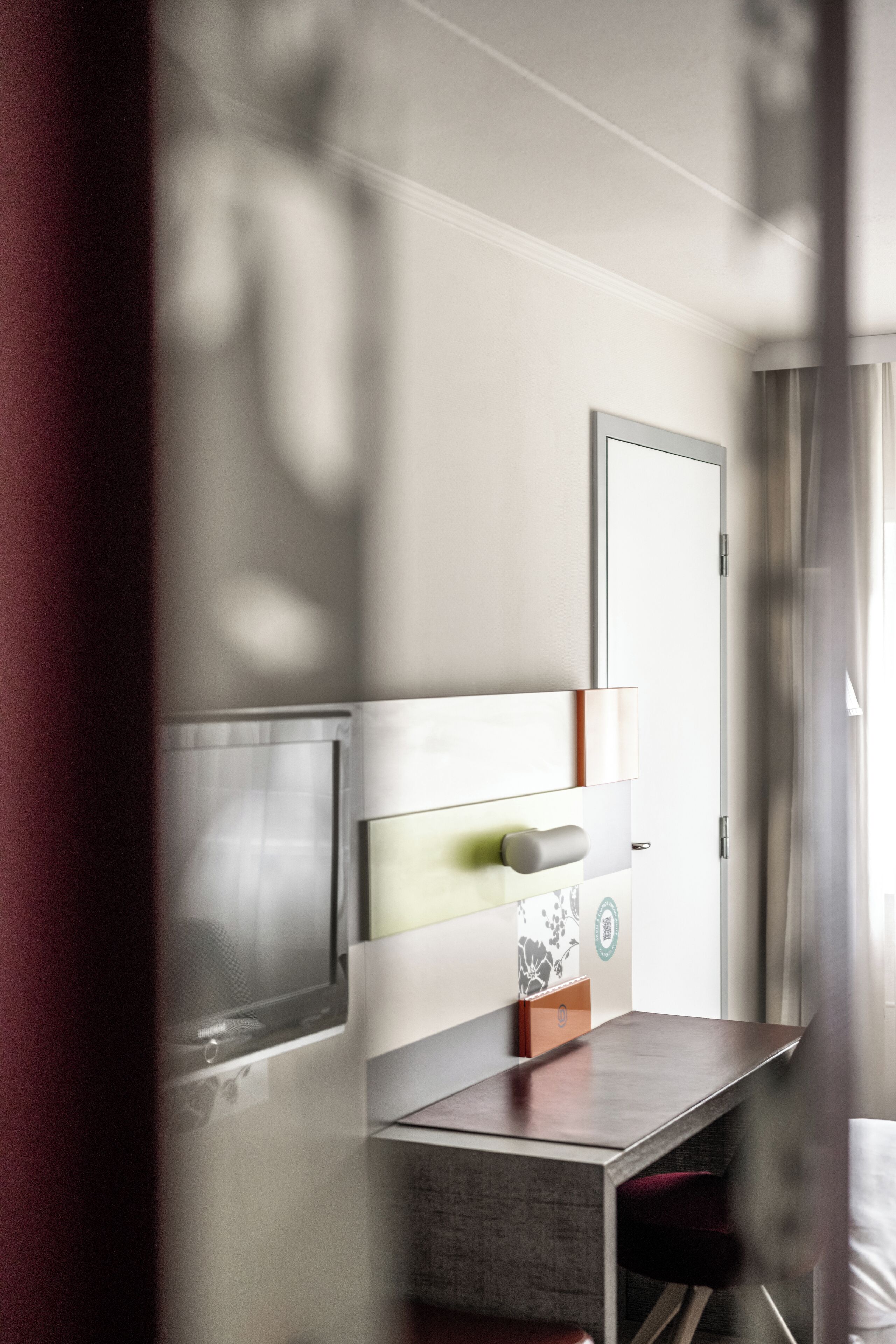 A modern hotel room with a flat-screen TV, a bedside table, a chair, and a door.