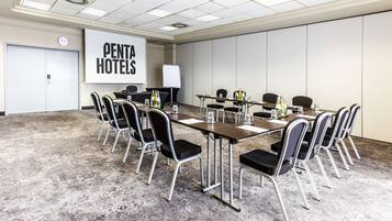 Uma sala de conferências com uma mesa comprida, cadeiras, um quadro branco e uma placa com a inscrição 'PENTA HOTELS'.