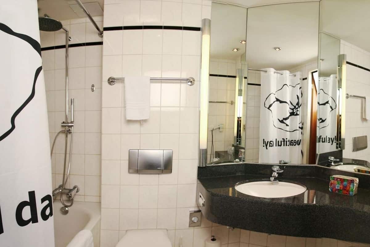 A modern bathroom with a large mirror, a sink, a shower, and a towel rack.