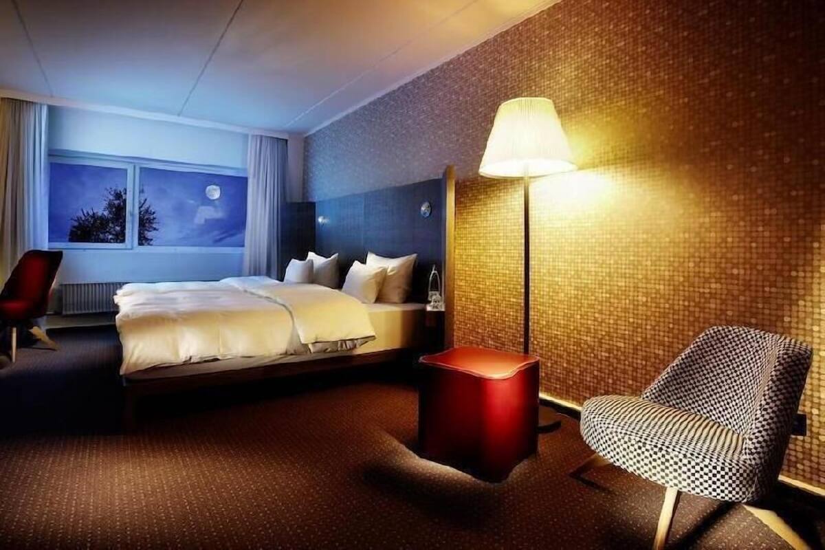 A hotel room with a bed, a chair, a nightstand, and a lamp.