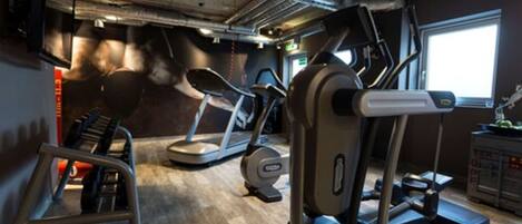 Un gimnasio con cintas de correr, elípticas y un banco para pesas.