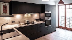 Una cucina moderna con mobili scuri, un lavello in acciaio inossidabile, forno integrato e illuminazione a sospensione.