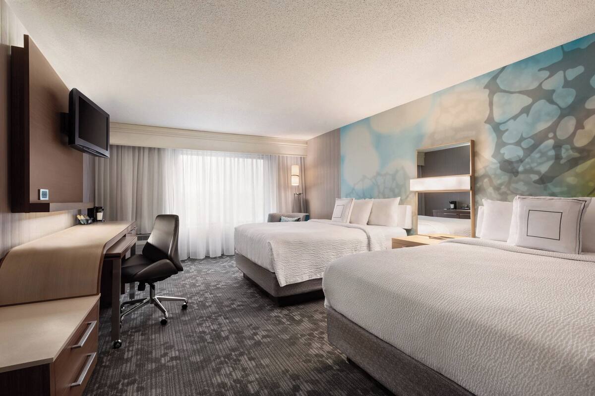 A hotel room with two beds, a desk, a chair, a TV, and a painting on the wall.