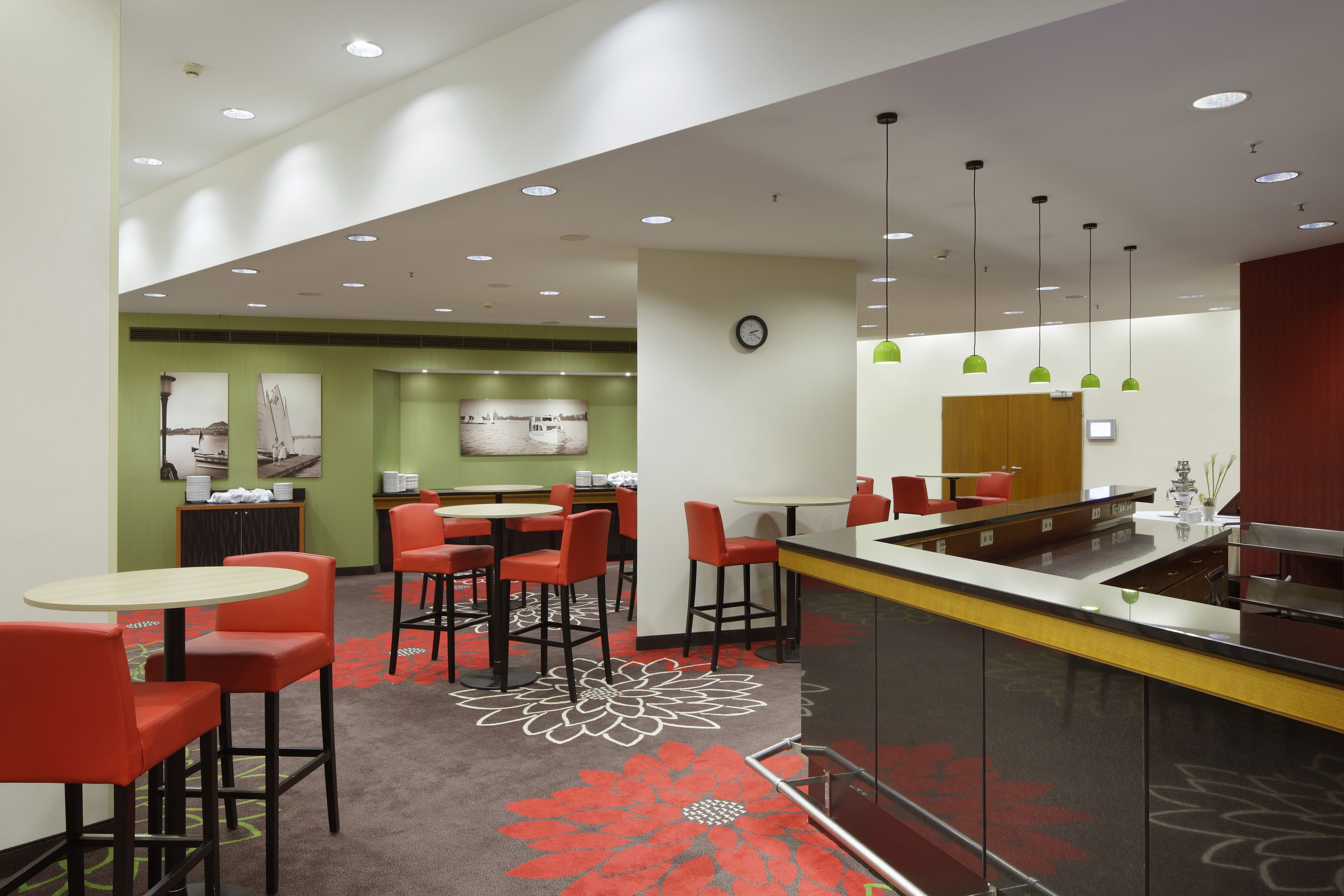 Una hall d'hotel moderna con area bar, sgabelli rossi e un motivo a fiori sul tappeto.