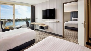 A hotel room with two beds, a TV, a desk, and a view of a river. - Courtyard by Marriott Hannover Maschsee (Hannover)