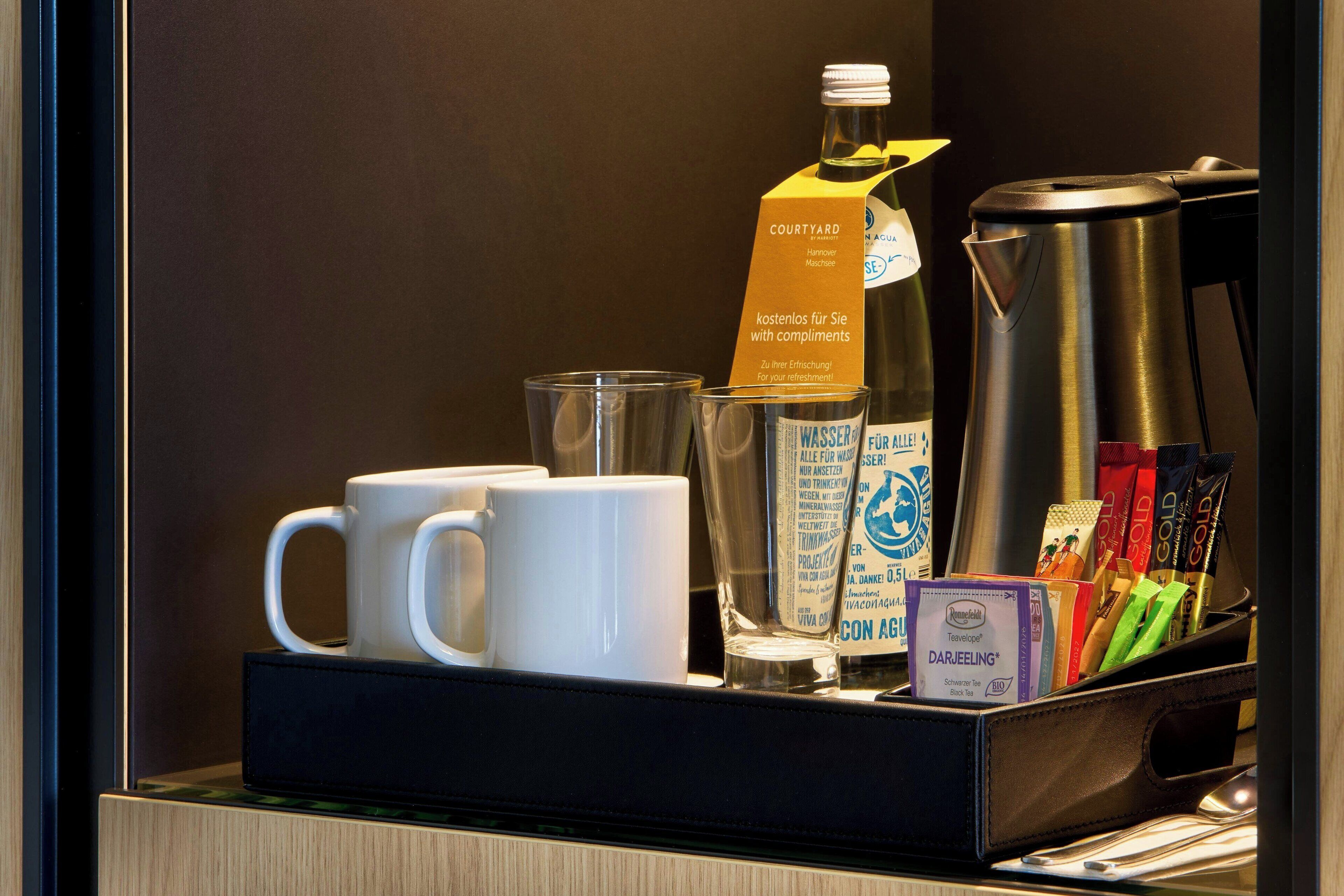 A coffee station with a coffee maker, cups, a glass, and coffee packets.