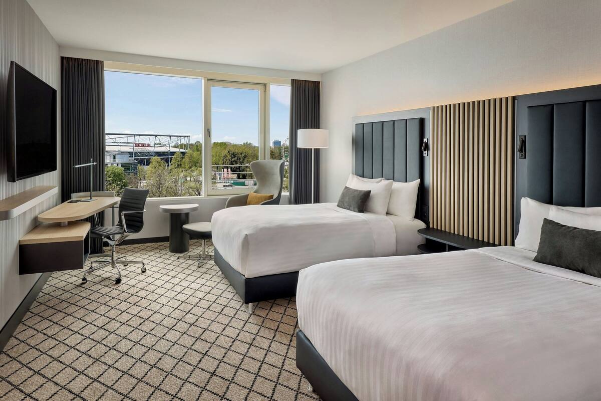 A hotel room with two beds, a desk, a chair, and a TV.