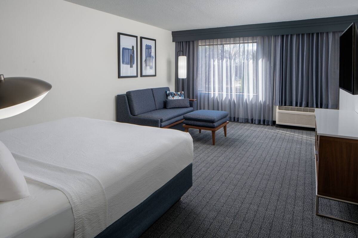 Quarto de hotel com uma cama grande, um sofá, uma mesinha e uma televisão.