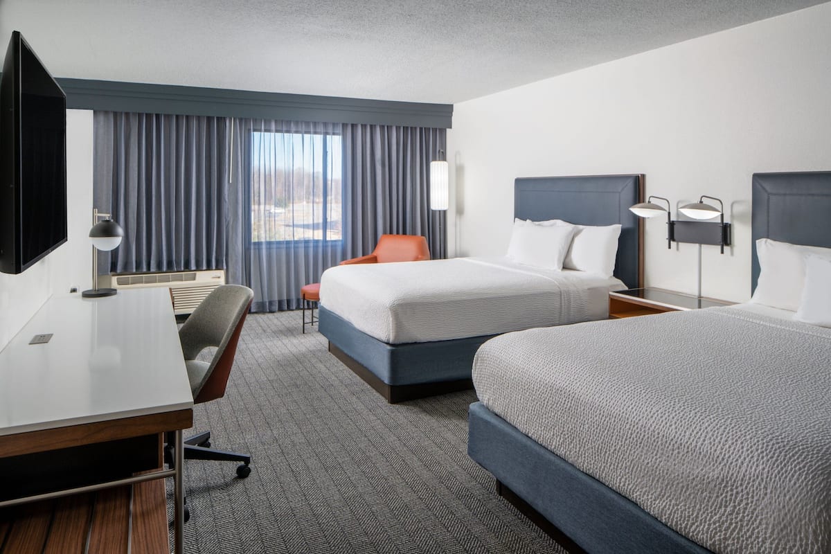 Quarto de hotel com uma cama grande, uma escrivaninha, uma cadeira e uma televisão.