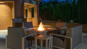 An outdoor patio with wicker furniture, a central fire pit, and a brick wall.