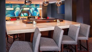 Un moderno hall de hotel con un amplio mostrador de recepción de mármol, sillones tapizados en gris y un gran mural abstracto en la pared.
