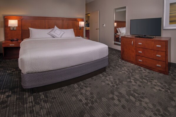 A hotel room with a large bed, a wooden headboard, a dresser with drawers, a television on the dresser, and a carpeted floor. - Courtyard by Marriott Dulles Town Center (Sterling)