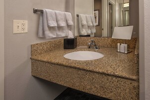 Un baño con lavamanos de encimera de granito, un espejo, toallero, dispensador de pañuelos y un interruptor de luz.