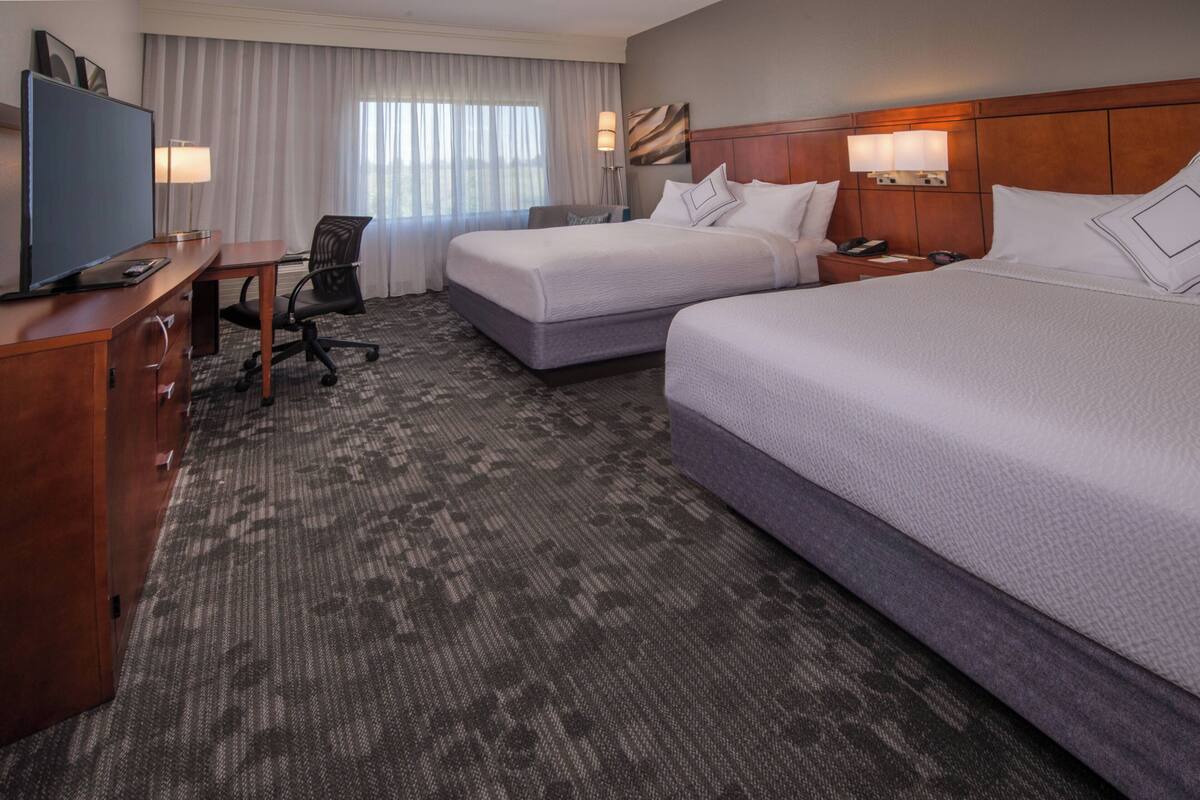 A hotel room with two beds, a desk, a television, and a lamp.