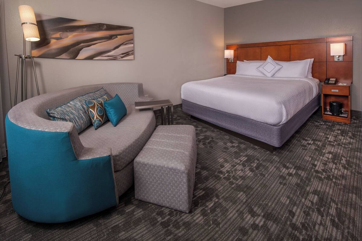 A hotel room with a large bed, a curved seating area, a small table, and a floor lamp.