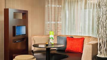 Una habitación de hotel moderna con un sofá, una mesa redonda, un televisor y una planta decorativa.