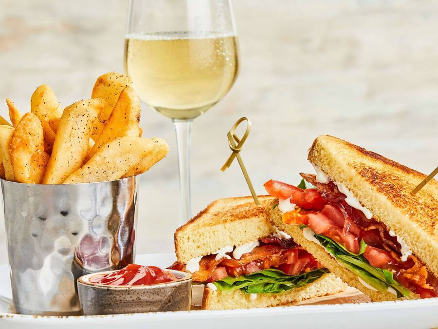 Un sandwich accompagné d’une portion de frites et d’un verre de vin blanc.