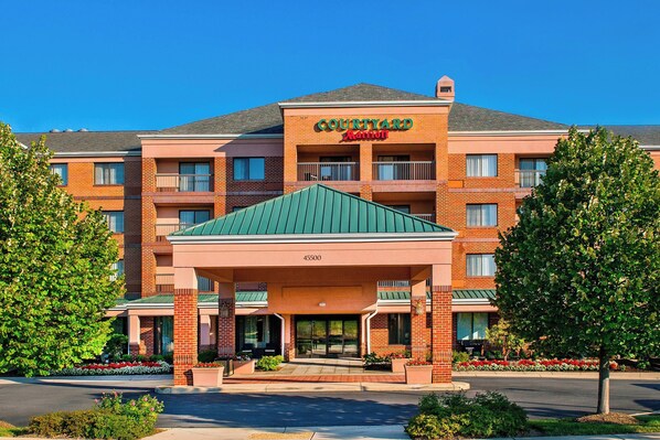A Courtyard by Marriott hotel with a brick facade, multiple balconies, and a green roof. - Courtyard by Marriott Dulles Town Center (Sterling)